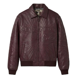 May include: A burgundy leather jacket with a zip-up front, collar, and ribbed cuffs and hem. The jacket features the embossed text "Avirex 50" across the chest and "Avirex" on the sleeves, with a sunburst design radiating from the center.