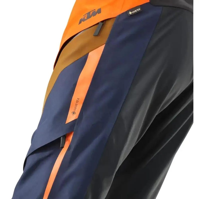 Puede incluir: Primer plano de una chaqueta multicolor. La chaqueta presenta paneles naranjas, marrones, azul marino y negros. Los paneles naranjas tienen el texto "GORE-TEX" y "KTM". La chaqueta est&aacute; dise&ntilde;ada para actividades al aire libre.
