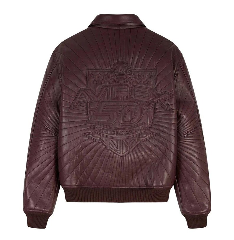 May include: A burgundy leather bomber jacket with a ribbed collar, cuffs, and hem. The back features an embossed design with the text "AVIREX 50 GOLD KICKOFF NY" within a sunburst pattern. The jacket has a classic, sporty style.