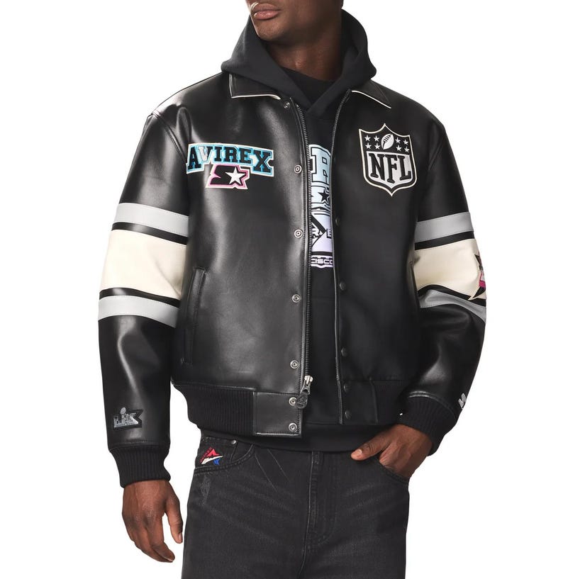 May include: Black leather jacket with white and gray striped sleeves. Features the NFL logo and Avirex patches. The jacket has a zip-up front and a ribbed hem and cuffs. The model is wearing a black hoodie underneath.