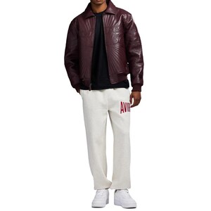 May include: A burgundy leather jacket with a quilted design and a black t-shirt. The person is wearing light gray sweatpants with the word "AVIR" in red letters. White sneakers complete the outfit.