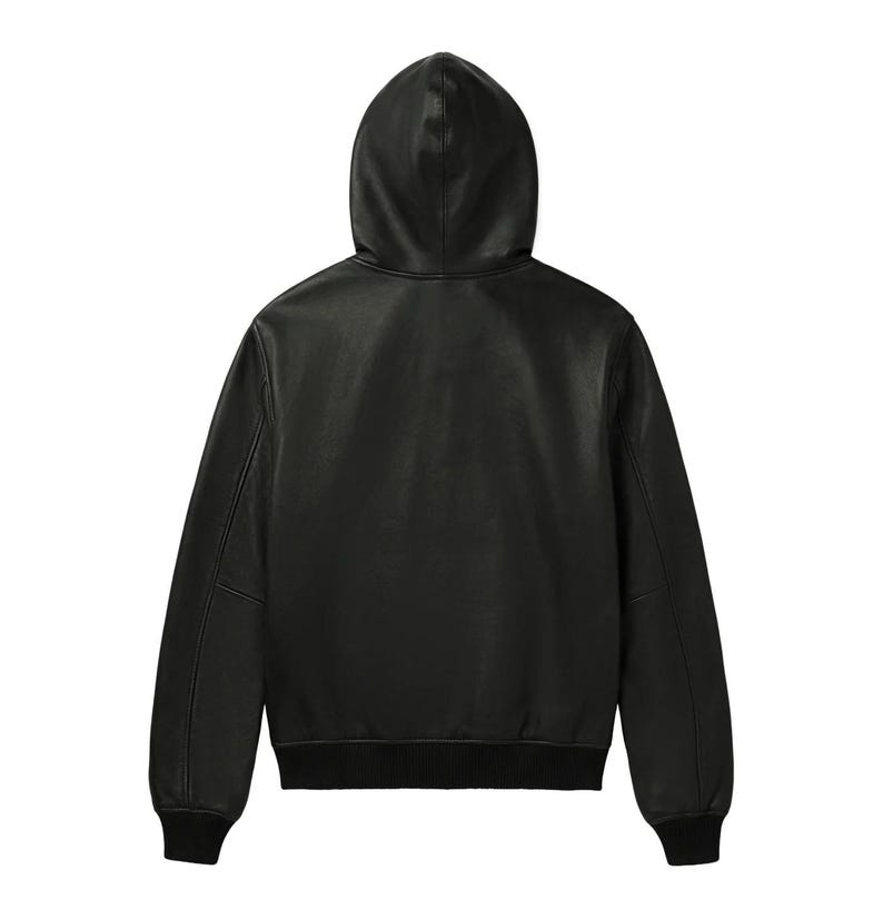 Pu&ograve; includere: Giacca con cappuccio in pelle nera con orlo e polsini a coste. La giacca ha una cerniera a tutta lunghezza e un cappuccio. La vista posteriore mostra il design e le cuciture. Un capo di abbigliamento classico.