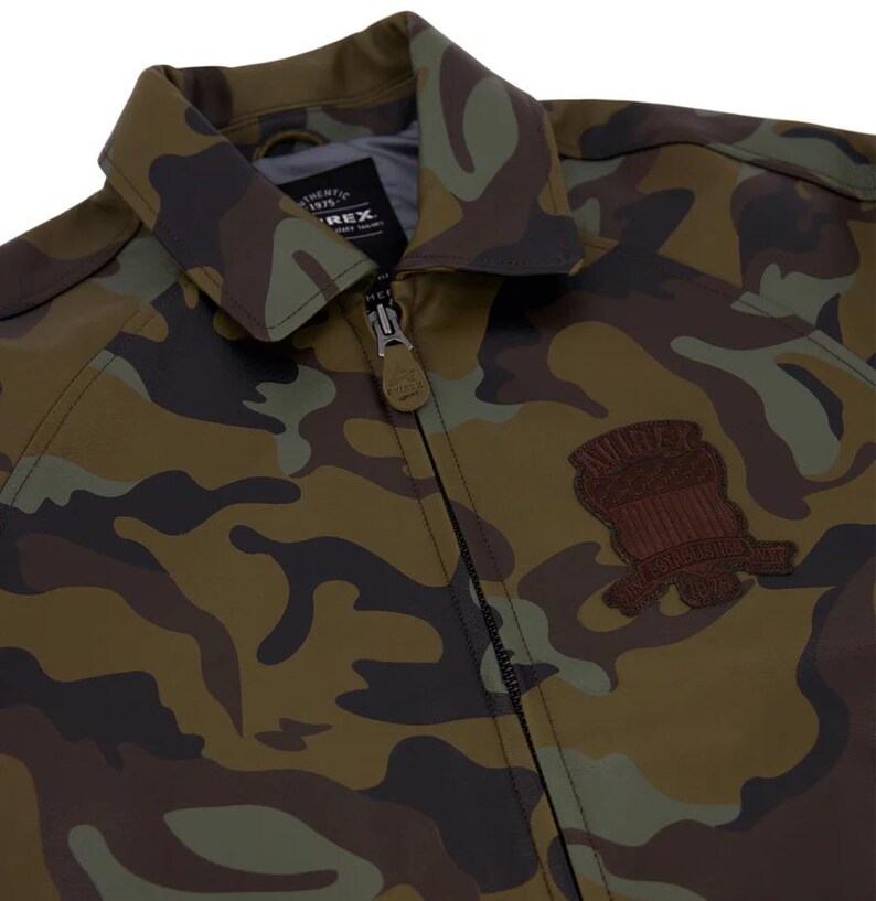 May include: Camouflage pattern jacket with a zipper closure and a collared neckline. The jacket features a brown patch on the chest. The color palette includes shades of green, brown, and black.