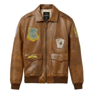 Pu&ograve; includere: Giacca bomber in pelle marrone con diverse toppe, tra cui uno scudo con testo e un disegno di carte da gioco. La giacca ha una chiusura con zip, due tasche frontali e polsini e orlo a coste. Il colletto mostra il marchio "AVIREX".