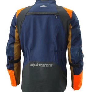 Puede incluir: Chaqueta de moto azul marino y naranja con detalles en negro. La chaqueta presenta el logotipo de KTM en la parte superior de la espalda y el logotipo de Alpinestars en la parte inferior. Tiene paneles naranjas en hombros y mangas.