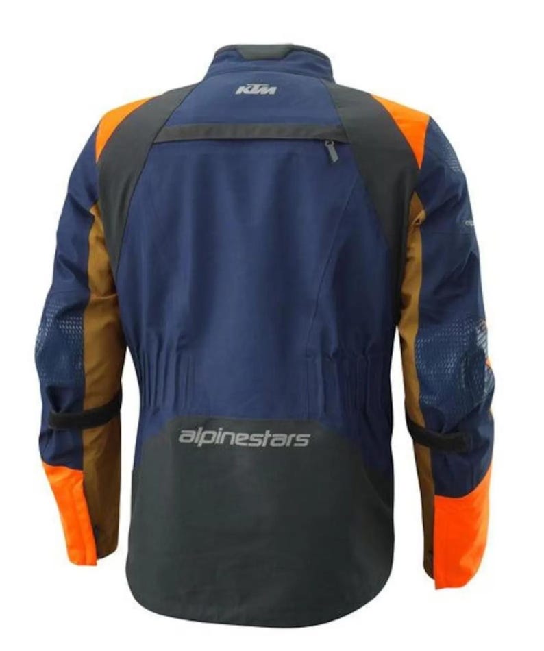 Puede incluir: Chaqueta de moto azul marino y naranja con detalles en negro. La chaqueta presenta el logotipo de KTM en la parte superior de la espalda y el logotipo de Alpinestars en la parte inferior. Tiene paneles naranjas en hombros y mangas.