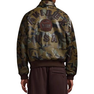 May include: Camouflage-patterned leather jacket with the text "AVIREX USA" on the back. The jacket features a brown ribbed collar, cuffs, and hem. The camouflage design incorporates shades of green, brown, and black.