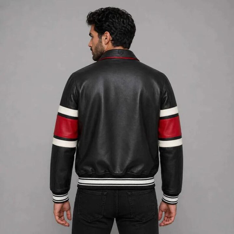 Pu&ograve; includere: Giacca in pelle nera con maniche a righe rosse e bianche e orlo a righe bianche e nere. La giacca ha un colletto rosso e un classico design da bomber. Il modello indossa jeans neri.