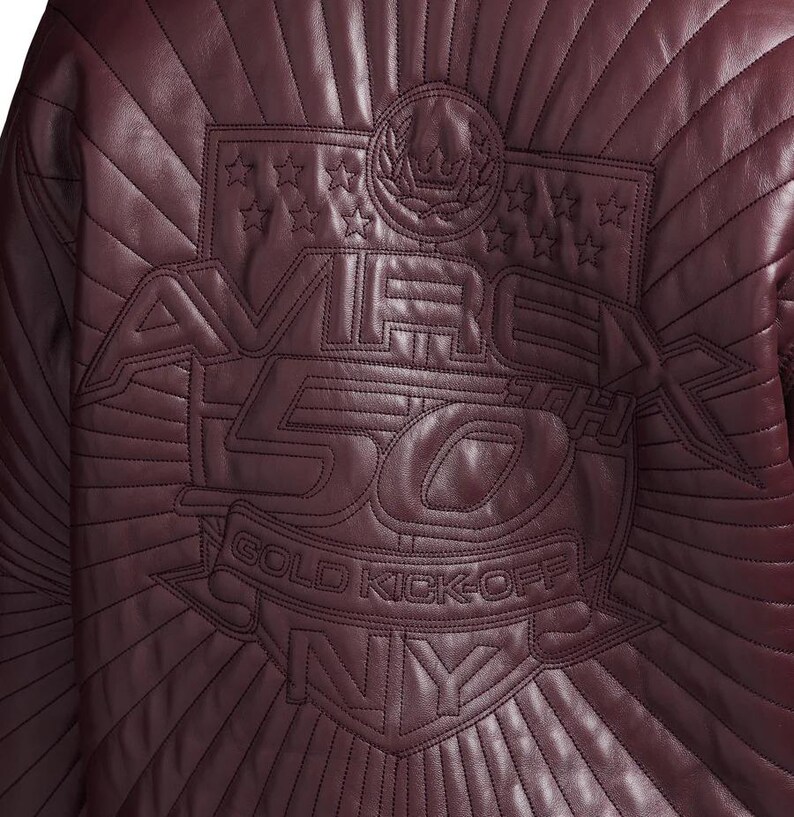May include: Burgundy leather jacket with quilted stitching. The back features an embossed design with the text "AVIREX 50TH GOLD KICK-OFF NY" and star and crown emblems.