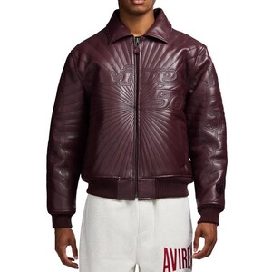 May include: A burgundy leather jacket with a zip-up front and a collar. The jacket features embossed text that reads "Divine 50" on the chest and sleeves. The jacket has a ribbed hem and cuffs.