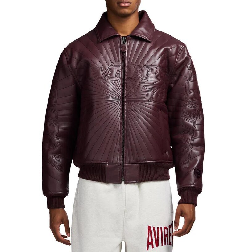 May include: A burgundy leather jacket with a zip-up front and a collar. The jacket features embossed text that reads "Divine 50" on the chest and sleeves. The jacket has a ribbed hem and cuffs.