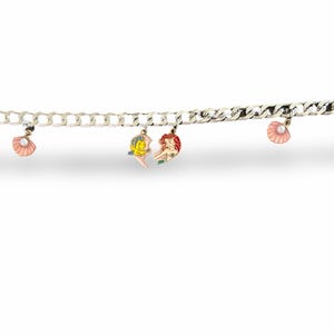 Peut inclure: Bracelet &agrave; cha&icirc;ne argent&eacute;e orn&eacute; de breloques en forme de coquillages, d'&eacute;toiles de mer et de sir&egrave;nes. Les breloques sont roses, oranges, jaunes et rouges. Fermoir mousqueton.