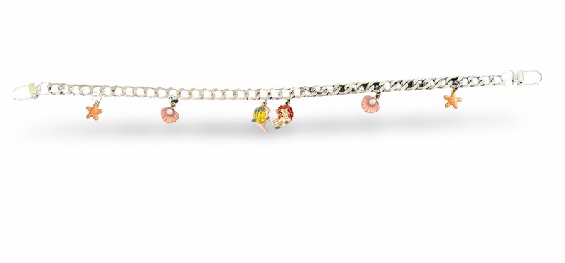 Peut inclure: Bracelet &agrave; cha&icirc;ne argent&eacute;e orn&eacute; de breloques en forme de coquillages, d'&eacute;toiles de mer et de sir&egrave;nes. Les breloques sont roses, oranges, jaunes et rouges. Fermoir mousqueton.