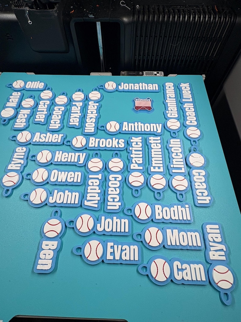 Pu&ograve; includere: Una collezione di portachiavi personalizzati azzurri con una grafica da baseball bianca con cuciture rosse e un nome o titolo stampato in lettere bianche. I nomi includono Ollie, Jonathan, Nate, Nash, Carter, Coach, Parker, Jackson, Anthony, Asher, Brooks, Ryne, Henry, Owen, Teddy, John, Ben, Evan, Patrick, Emmett, Lincoln, Gianfranco, Coach Lueck, Bodhi, Mom, Ryan e Cam.