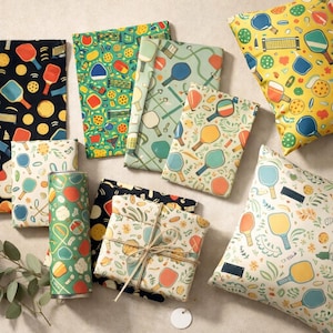 May include: An assortment of patterned fabric and pillows featuring pickleball paddles and balls in various colors. Designs include yellow, green, blue, and orange paddles on black, white, and green backgrounds. A cylindrical container is also visible.