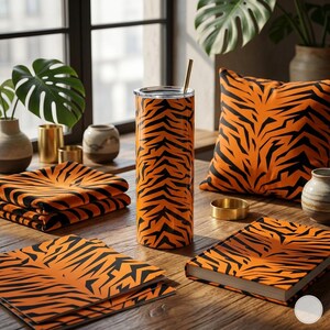 May include: An orange and black tiger stripe pattern is featured on a tumbler, pillow, napkins, and a book. A gold straw is in the tumbler. The items are on a wooden table with plants and decorative vases in the background.