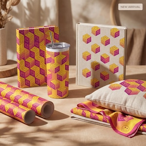 May include: Various items with a repeating cube pattern of yellow and pink smiley faces. The items include a tumbler, journal, pillow, scarf, and rolls of wrapping paper. The background is a light brown surface.