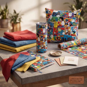 May include: A collection of Japanese pop art items, including a tumbler, pillow, notebook, and rolled paper, all featuring colorful comic book-style illustrations. Also includes folded linen cloths in red, blue, and yellow, and small cards. The items are arranged on a concrete surface.