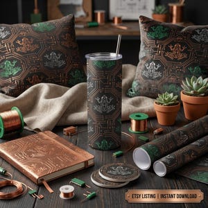 Op de afbeelding: Een verzameling woondecoratieartikelen met een printplaat- en kikkerontwerp. Inclusief kussens, een tumbler, onderzetters, een notitieboek en inpakpapier. Het kleurenschema is bruin, groen en koper. De items zijn gerangschikt op een donker houten oppervlak.