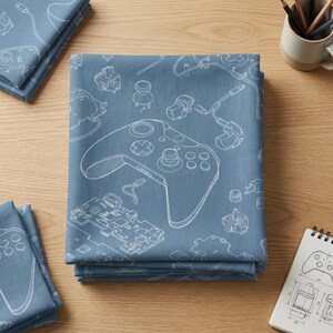 May include: Blue bedding set with a white line drawing of a games controller and its components. The design includes the controller's buttons, circuit board, and other internal parts. The set is folded and stacked on a wooden surface.