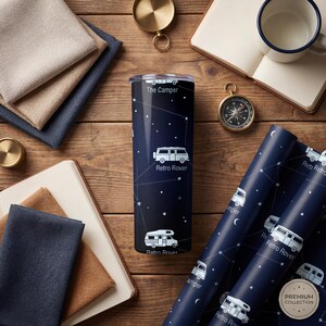 May include: A navy blue travel tumbler with the text "The Camper" and "Retro Rover" in white. The tumbler features a constellation design with white stars and camper van illustrations. Matching wrapping paper is also visible.