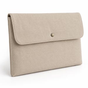 Peut inclure: Une pochette rectangulaire en tissu beige avec un rabat repliable et un bouton-pression métallique centré. La pochette présente un design structuré et épuré avec des coutures visibles le long des bords du rabat et du corps principal.