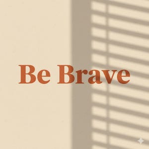 May include: A beige background with the words "Be Brave" in a burnt orange, serif font. The shadow of a window blind is cast across the upper right corner of the image.