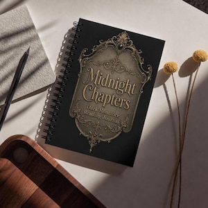 Op de afbeelding: Een zwart spiraalgebonden notitieboek met de titel "Midnight Chapters" in gouden letters. De omslag heeft een sierlijk gouden filigraan en de ondertitel "Dark Romance Reading Journal". Een potlood en notitieblok zijn zichtbaar op de achtergrond.