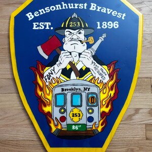 May include: A shield-shaped sign with a blue background and yellow trim. The sign features a cartoon firefighter with an axe and hose, the text "Bensonhurst Bravest," and "EST. 1896." A subway car graphic is also present, with the text "Brooklyn, NY" and "86".