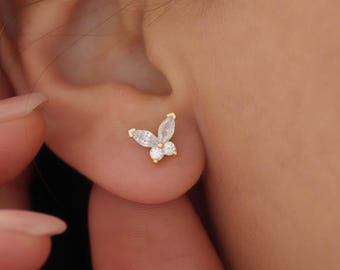 May include: A gold-colored butterfly stud earring with clear, sparkling crystals. The butterfly design features two elongated crystals for the wings and two round crystals for the body. The earring is shown on an ear.