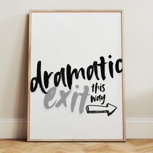 May include: A framed art print with the words "dramatic exit this way" in black and gray brush lettering. The arrow points to the right. The artwork is displayed on a white background.