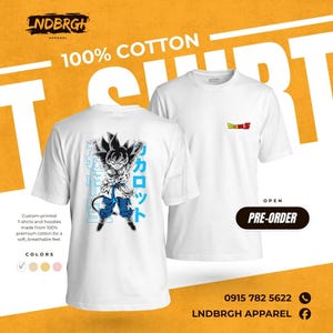 May include: A white short-sleeve t-shirt featuring a graphic of a black-haired anime character in a fighting stance on the back, with blue Japanese text. The front of the shirt displays a small Dragon Ball Z logo on the left chest area.