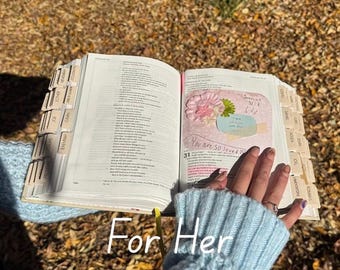 Puede incluir: Un libro abierto con pestañas etiquetadas, con una página decorada con una flor rosa y el texto "You are so loved". Las palabras "For Her" están escritas en la parte inferior de la imagen. El fondo es una vista borrosa de hojas de otoño.