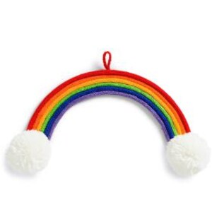 Könnte beinhalten: Gestrickte Regenbogen-Dekoration mit roten, orangefarbenen, gelben, grünen, blauen und violetten Bögen. Zwei weiße Pompons sind an den Enden befestigt. Oben befindet sich eine rote Schlaufe zum Aufhängen.