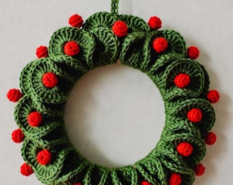 May include: A handmade green crochet wreath with red berry accents. The wreath is circular, with a loop for hanging. The red berries are evenly spaced around the wreath, adding a festive touch. Perfect for holiday decor.