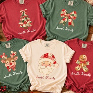 May include: Five short-sleeved t-shirts in red, green, and white featuring Christmas-themed patchwork graphics of a tree, bow, reindeer, Santa Claus, and gingerbread man, each with the embroidered text Smith Family below the design.