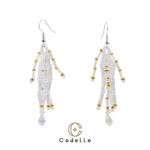 May include: A pair of handmade earrings featuring a skeleton design. The earrings are made of clear and gold beads, with a silver hook. The skeleton earrings have a dangling crystal at the bottom. The brand name "Codelle" is at the bottom.
