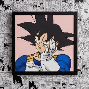 Może przedstawiać: Oprawiony portret w pikselach postaci z Dragon Ball Z, z czarnymi włosami, niebieskimi i białymi ubraniami oraz różowym tłem. Grafika jest umieszczona na tle czarno-białych paneli mangi.