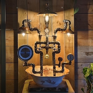 Op de afbeelding: Een unieke steampunk-stijl lamp met een bloemmotief bekken, pijpen, meters en klokken. De lamp heeft drie koperkleurige lampenkappen en een centraal licht. De armatuur is gemonteerd op een houten oppervlak.