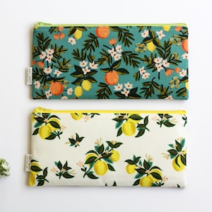 May include: Two zippered pouches with a lemon and floral print. The top pouch is teal with yellow lemons and orange flowers. The bottom pouch is white with yellow lemons and green leaves.
