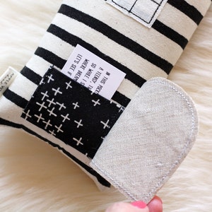 May include: A black and white striped pillow with a small pocket on the side. The pocket has a white fabric with a black cross pattern. A white tag is sticking out of the pocket with the text "IN THIS POCK A TEENSY, TH SO WHILE I S WHERE DREAM LET'S SEE IF". The pillow has a heart-shaped flap on the side.