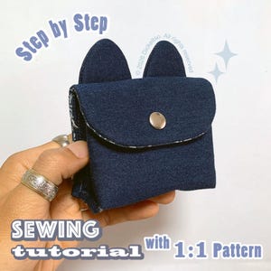 May include: A dark blue denim pouch featuring two rounded ears at the top and a silver metal snap button closure. The text "Step by Step", "SEWING tutorial with 1:1 Pattern", and "© 2026 Dickeltso. All rights reserved" is visible on the image.
