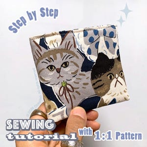May include: A square fabric pouch featuring a printed pattern of two cats, one grey tabby and one dark brown and white cat, against a dark blue background. The text "Step by Step" and "SEWING tutorial with 1:1 Pattern" is overlaid on the image.