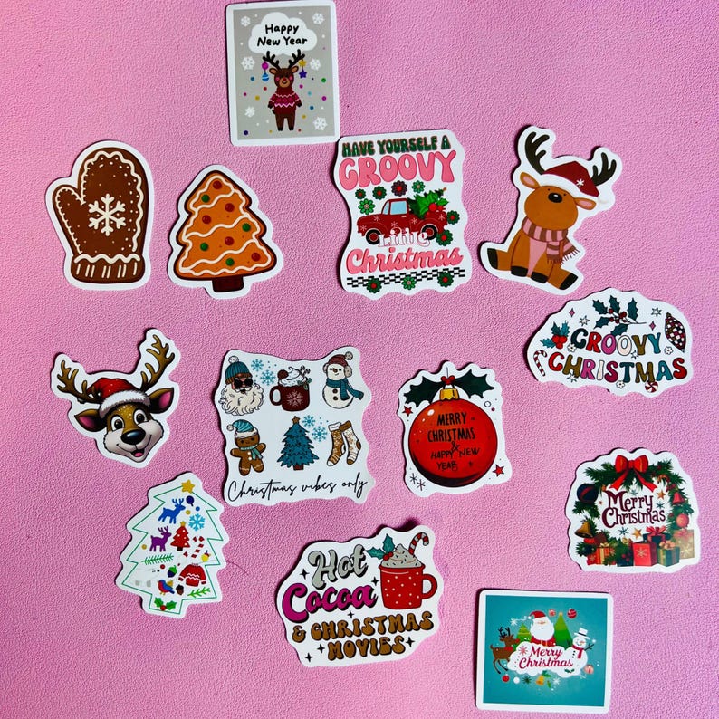 May include: A selection of Christmas stickers featuring festive designs. Includes reindeer, Christmas trees, and gingerbread men. Text includes "Merry Christmas" and "Hot Cocoa & Christmas Movies" on a pink background.