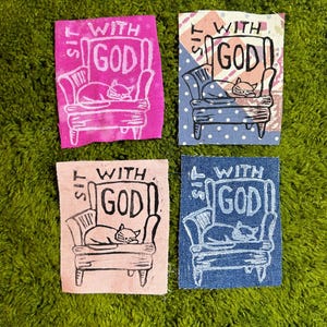 May include: Four fabric patches with a hand-drawn design. Each patch features a cat sleeping in a chair with the words "SIT WITH GOD". The patches are in pink, blue, and patterned fabrics.