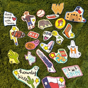 Puede incluir: Una colección de parches coloridos dibujados a mano con temática de Texas. Los diseños incluyen un vaquero, el Álamo, un balón de fútbol, una pelota de béisbol y la bandera del estado de Texas. El texto incluye "Howdy Y'all", "Don't mess with Texas".