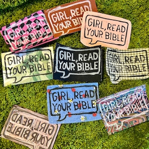 May include: A collection of handmade rectangular patches with the text "GIRL, READ YOUR BIBLE" in a speech bubble design. The patches feature various patterns and colors, including pink, brown, blue, and plaid.