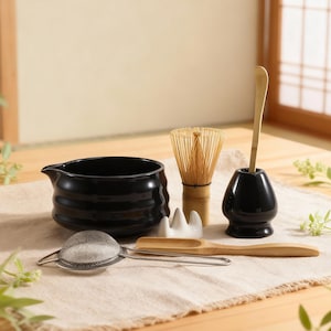 Könnte beinhalten: Ein schwarzes Keramik-Matcha-Schälchen mit Ausguss, ein Bambusbesen, ein Besenhalter, ein Bambuslöffel, ein Matcha-Sieb und ein Schneebesenhalter. Die Artikel sind auf einem beigen Leinentuch angeordnet, was auf ein Teezeremonie-Set hindeutet.