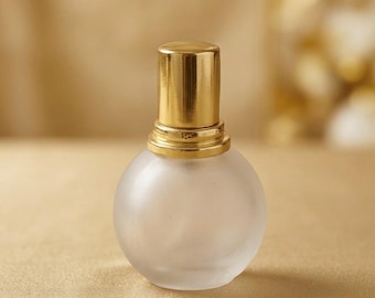 May include: A small, spherical perfume bottle made of frosted glass with a smooth, matte texture. The bottle features a cylindrical, polished gold-colored metal cap that sits securely on a matching gold-colored neck collar at the top of the vessel.