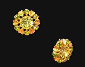Pendientes vintage firmados de Avon con pedrería verde, cierre de clip, botón con textura de hoja en tono dorado, joyería botánica retro de mediados de siglo.